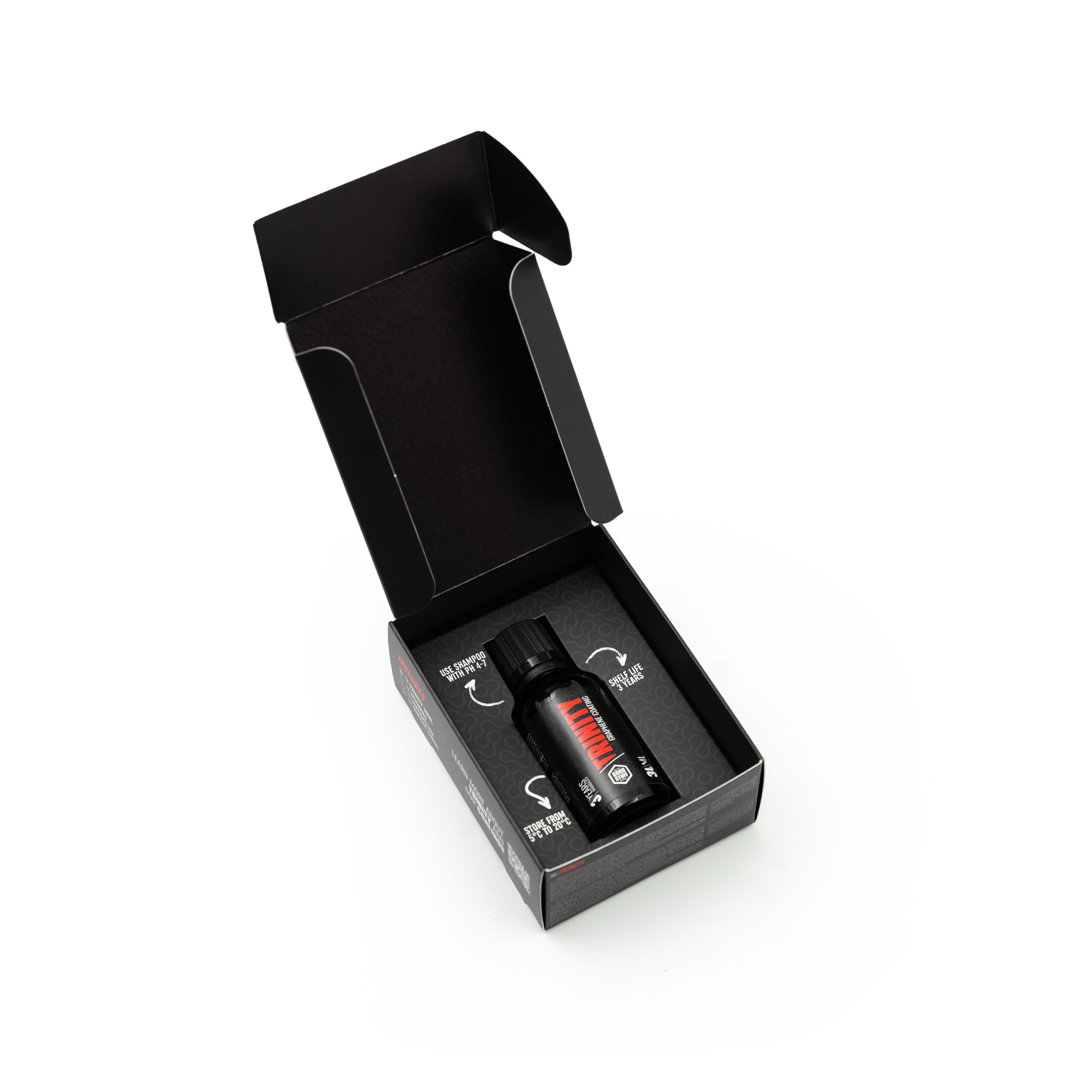 A small black bottle with a black cap placed inside an open black cardboard box, shown on a white background. The box features printed instructions and secure compartments for the bottle.