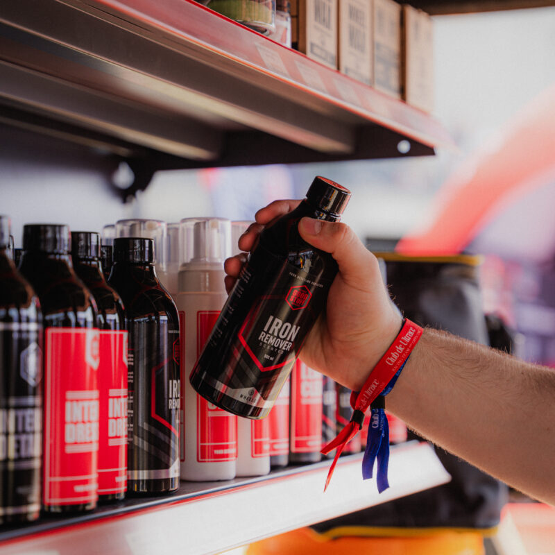 A person wearing colorful wristbands is holding a bottle labeled Iron Remover from a shelf stocked with various car care products, perfect for those looking to place orders or start cooperation in the car care business.