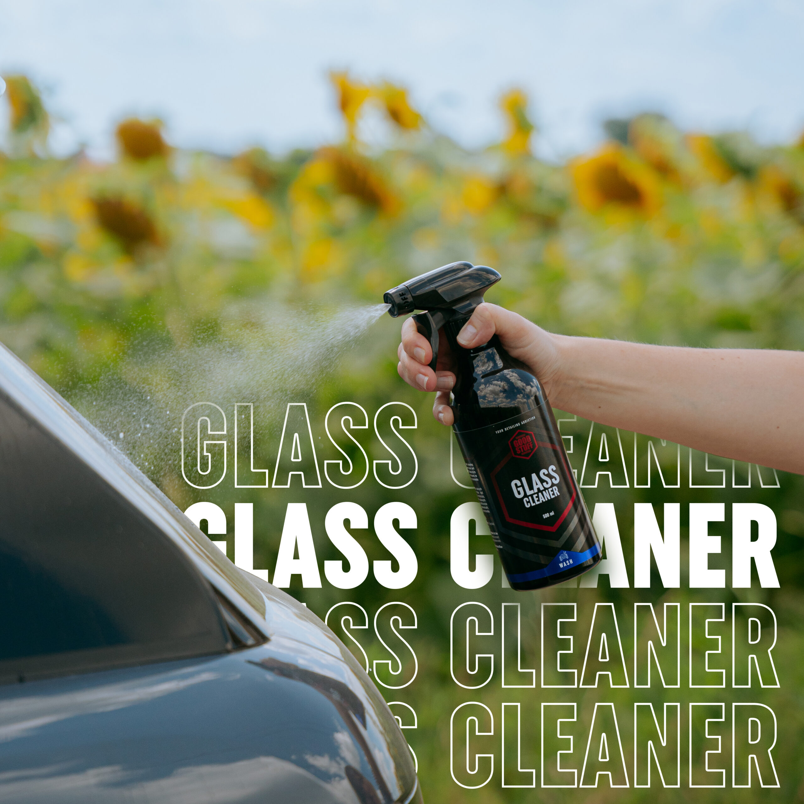 A hand sprays streak-free cleaner onto a car window outdoors, with sunflowers and greenery in the background. The words GLASS CLEANER are repeatedly overlaid in bold white text.