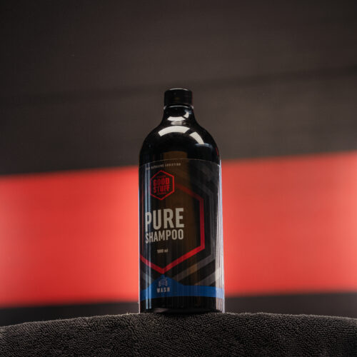 A black bottle of Pure Shampoo by Good Vibes, also known as a premium car shampoo, sits on a dark towel, with a blurred red and black background.