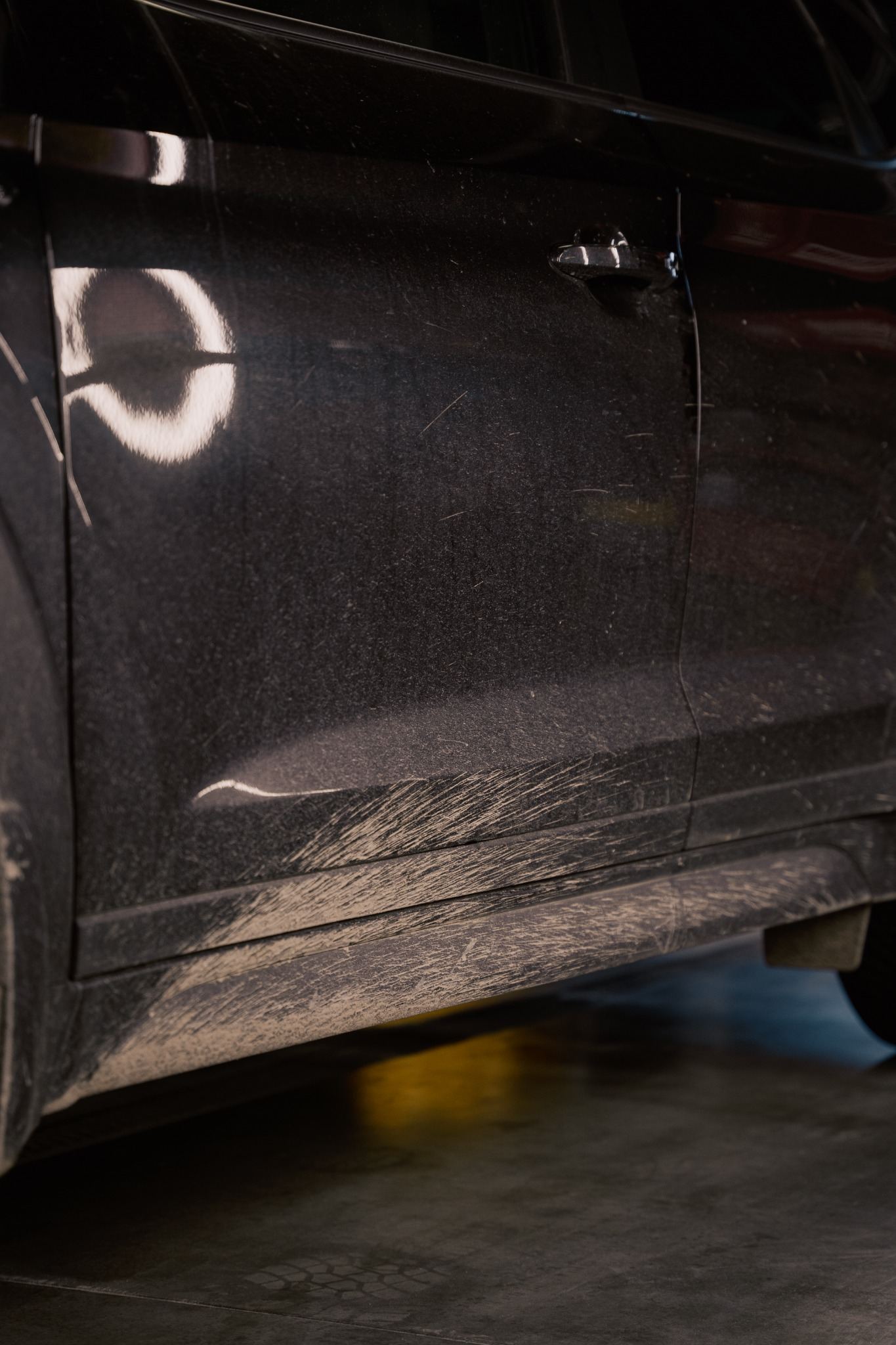Close-up of heavy traffic film and road grime on a car lower door and sill